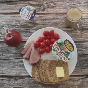 Zdjęcie przedstawia Dietę z ograniczeniem łatwoprzyswajalnych węglowodanów: Chleb Graham Masło extra Serek wiejski ziarnisty Kawa zbożowa z mlekiem Jogurt naturalny Woda źródlana Sałata zielona Pomidorki koktajlowe Szynka Piastowska